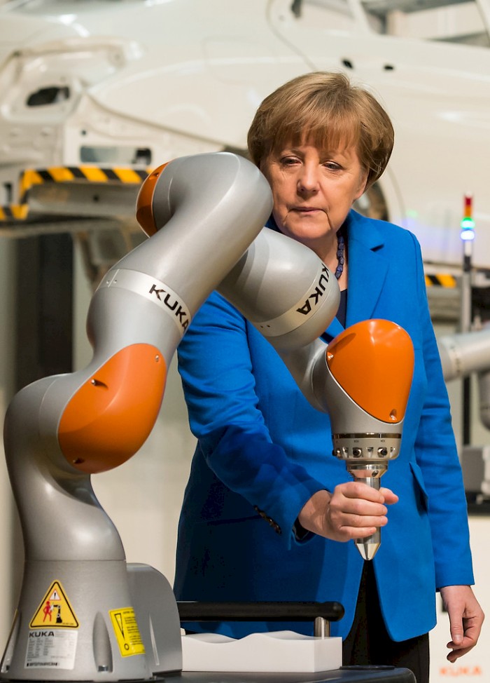 German Chancellor Angela Merkel tests a robotic arm while visiting one of the leading producers of industrial robots in the KUKA factory in Augsburg, Germany. The <em>New York Times</em> recently referenced the company in its coverage of the increasing automation of assembly lines in China. See <a  data-cke-saved-href="http://www.nytimes.com/2015/04/25/technology/robotica-cheaper-robots-fewer-workers.html?_r=0" href="http://www.nytimes.com/2015/04/25/technology/robotica-cheaper-robots-fewer-workers.html?_r=0" target=“new”>→</a>